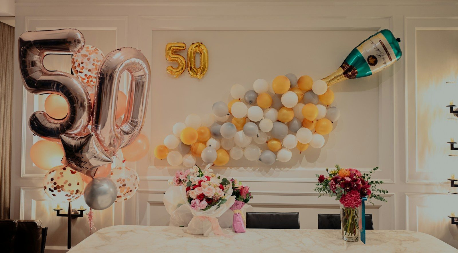 Phòng tiệc sinh nhật tuổi 50 với bóng bay số 50, tường bóng bay vàng trắng và hoa trên bàn trắng