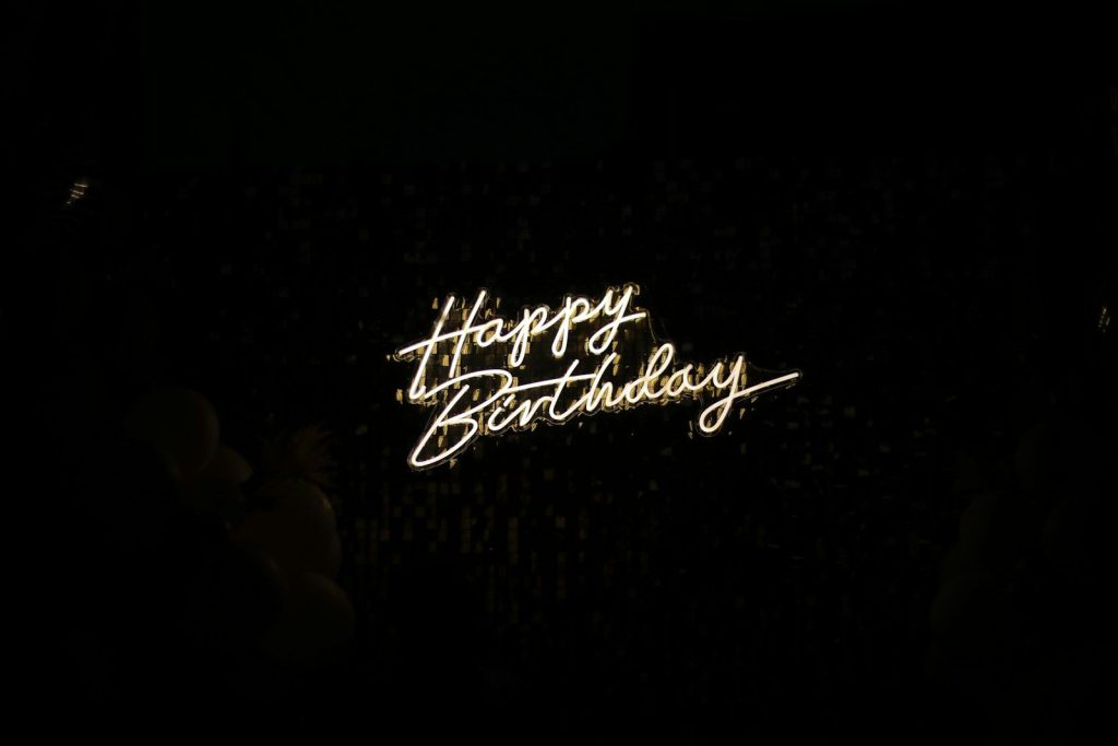 Biển đèn neon chữ Happy Birthday màu vàng ấm gắn trên một bức tường tối