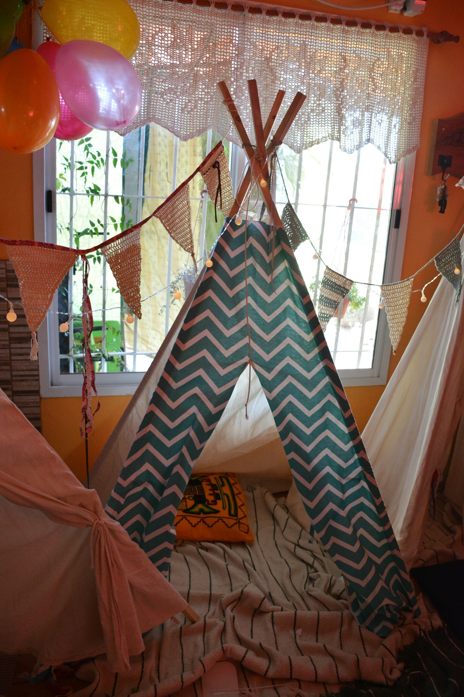 Lều chơi kiểu teepee cạnh bóng bay và dây cờ trong một căn phòng đầy nắng